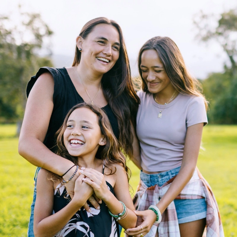 Hawaii Family SQ 3 Hawaiʻi Family with mom and two daughters laughing in a yard.