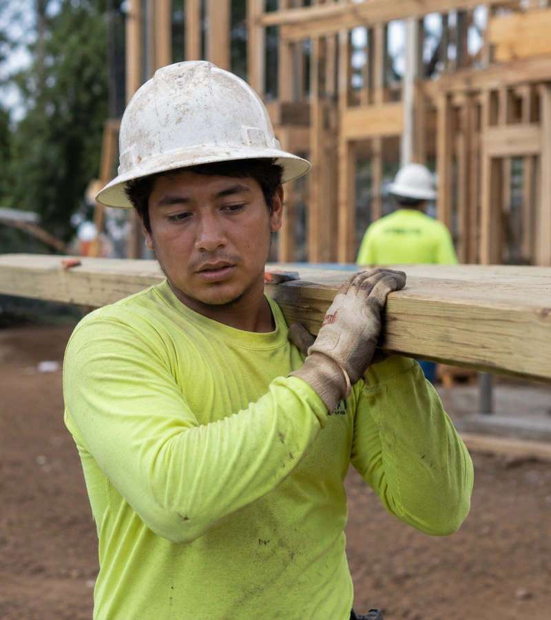 young construction worker carries a beam